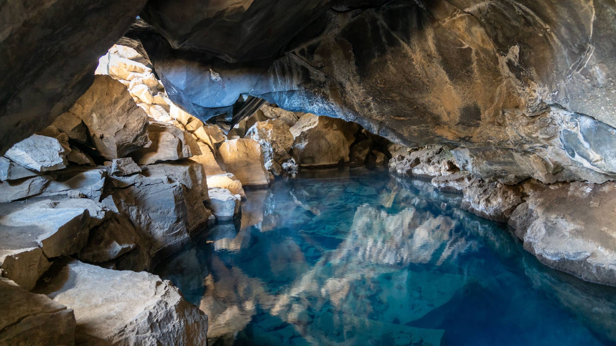 Blue geothermal water and rough lava walls inside Grjótagjá cave near Lake Mývatn.