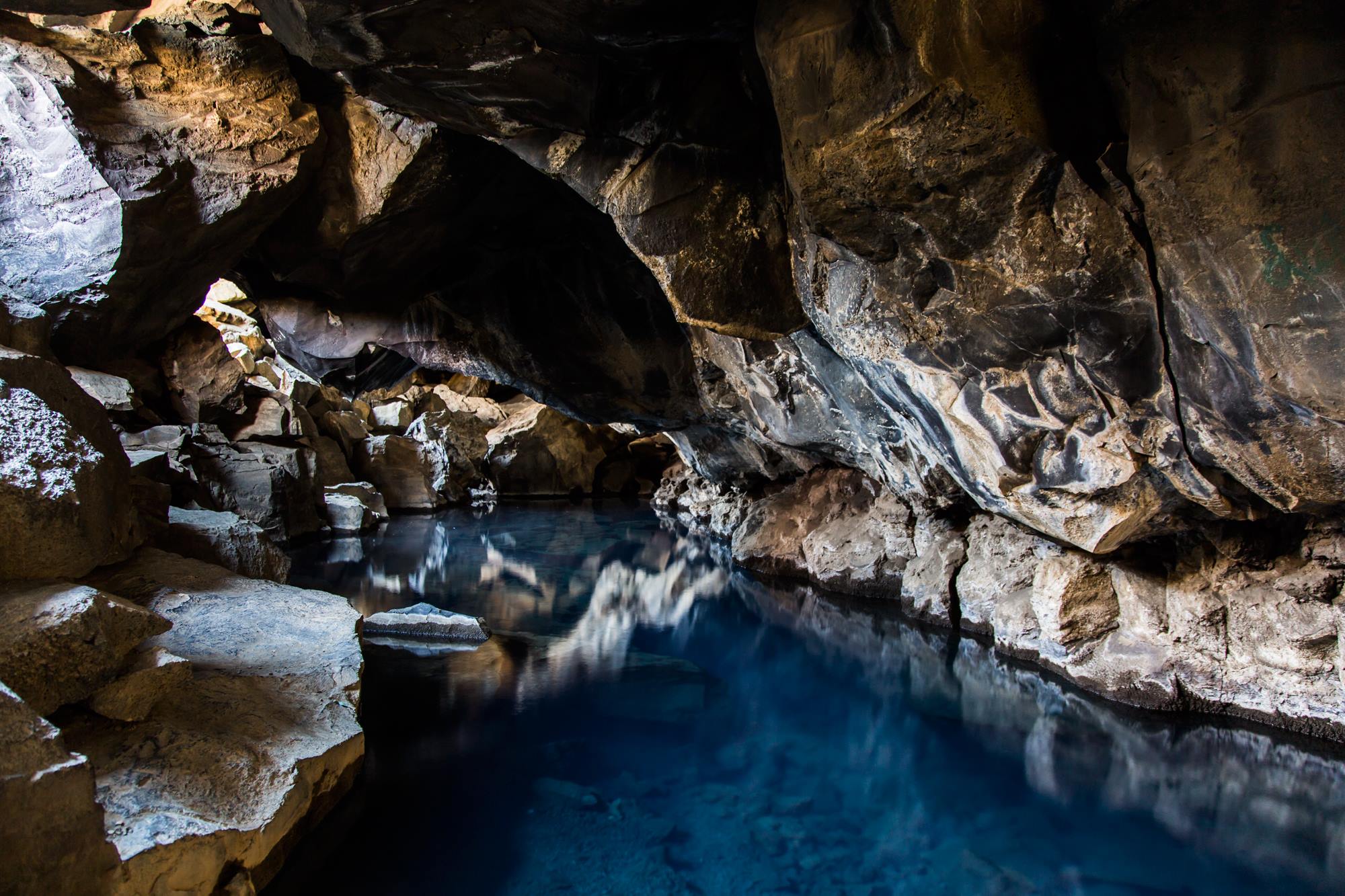 Blue geothermal water below a dark lava ceiling inside Grjótagjá cave near Lake Mývatn.