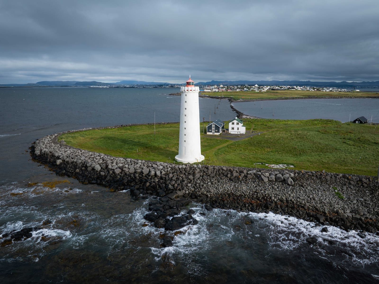 Grótta lighthouse on its tidal islet with Reykjavík and mountains beyond the water