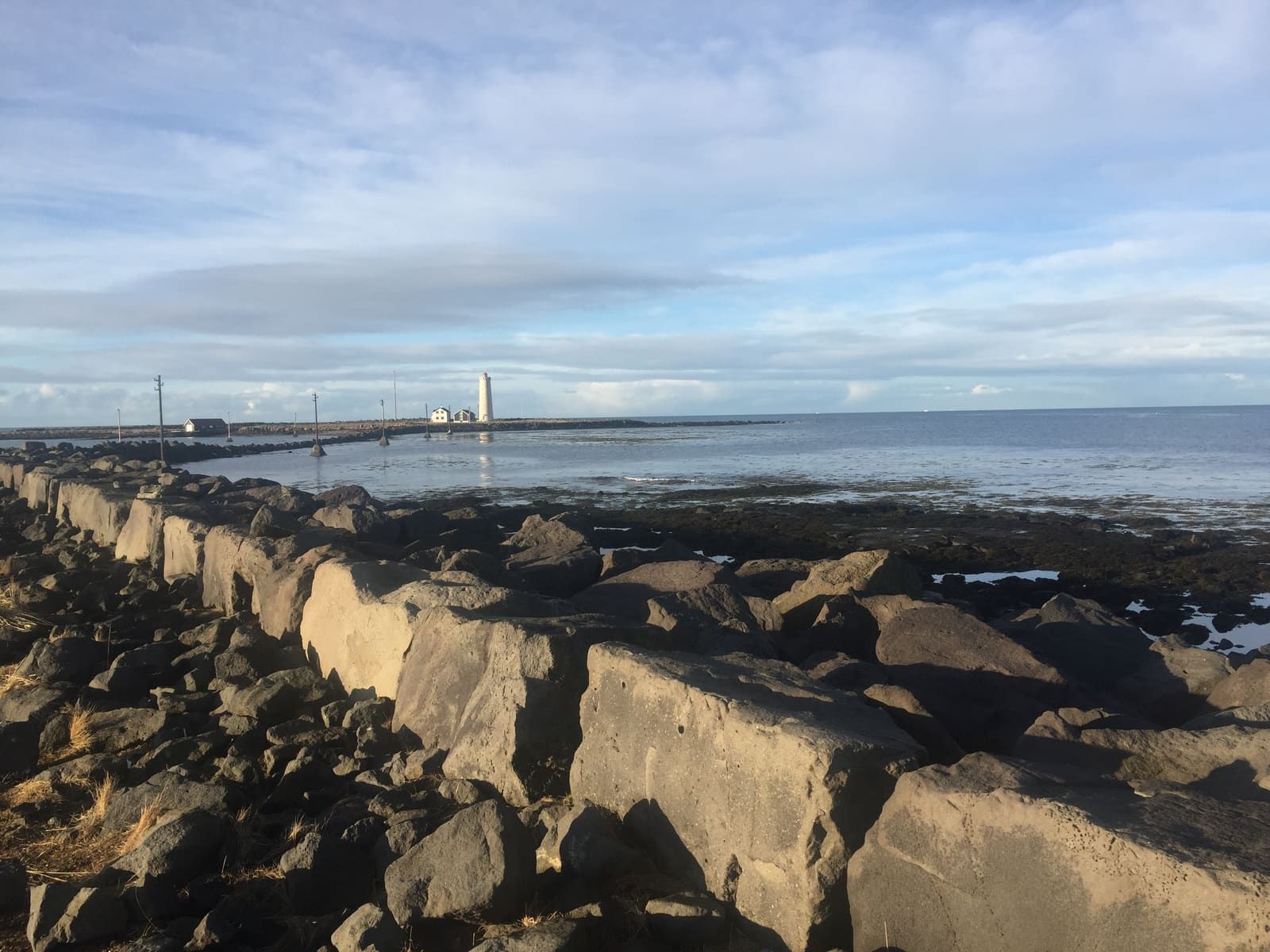 Rocky Seltjarnarnes shoreline with Grótta lighthouse across shallow tidal water