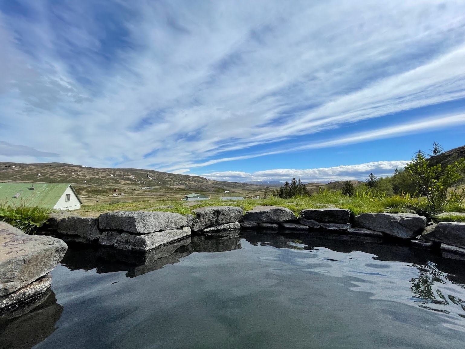 Guðrúnarlaug stone pool edge with dark water and the Sælingsdalur valley beyond.