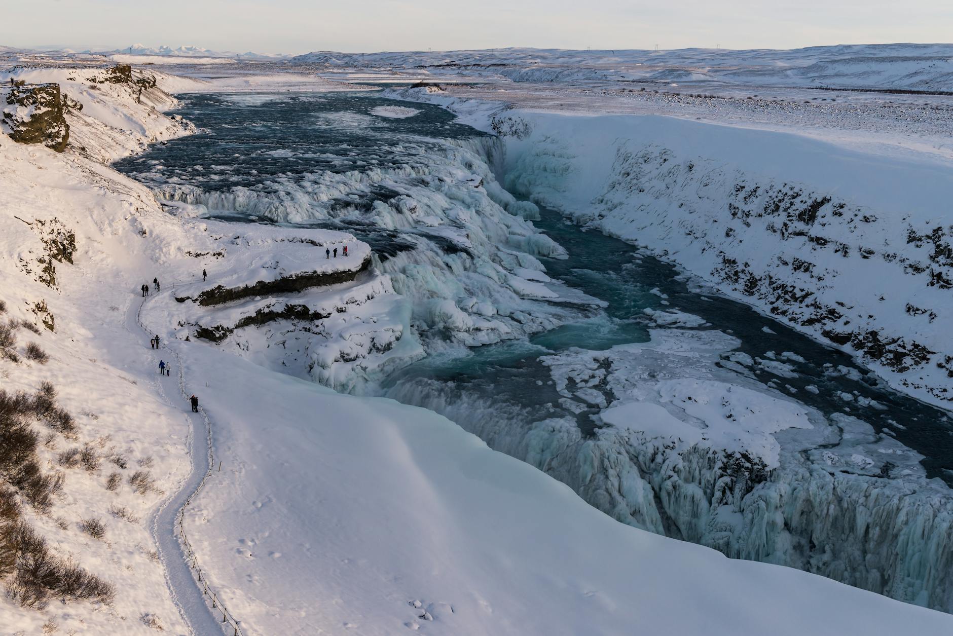 Winter view over Gullfoss with people on the marked viewpoint path above the canyon.