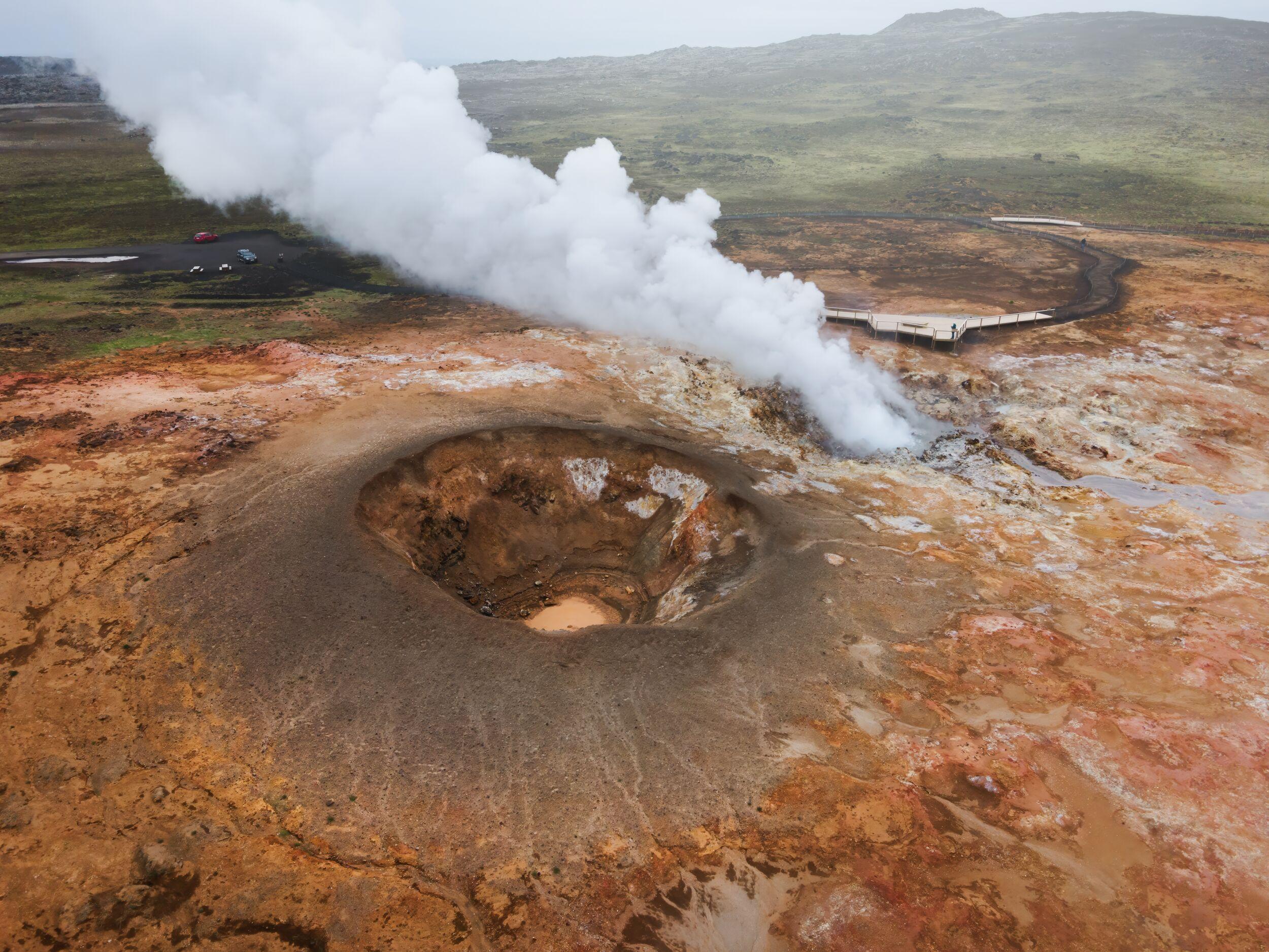 Aerial view of Gunnuhver with a large mud pool, steam plume, boardwalks, and colored geothermal ground.