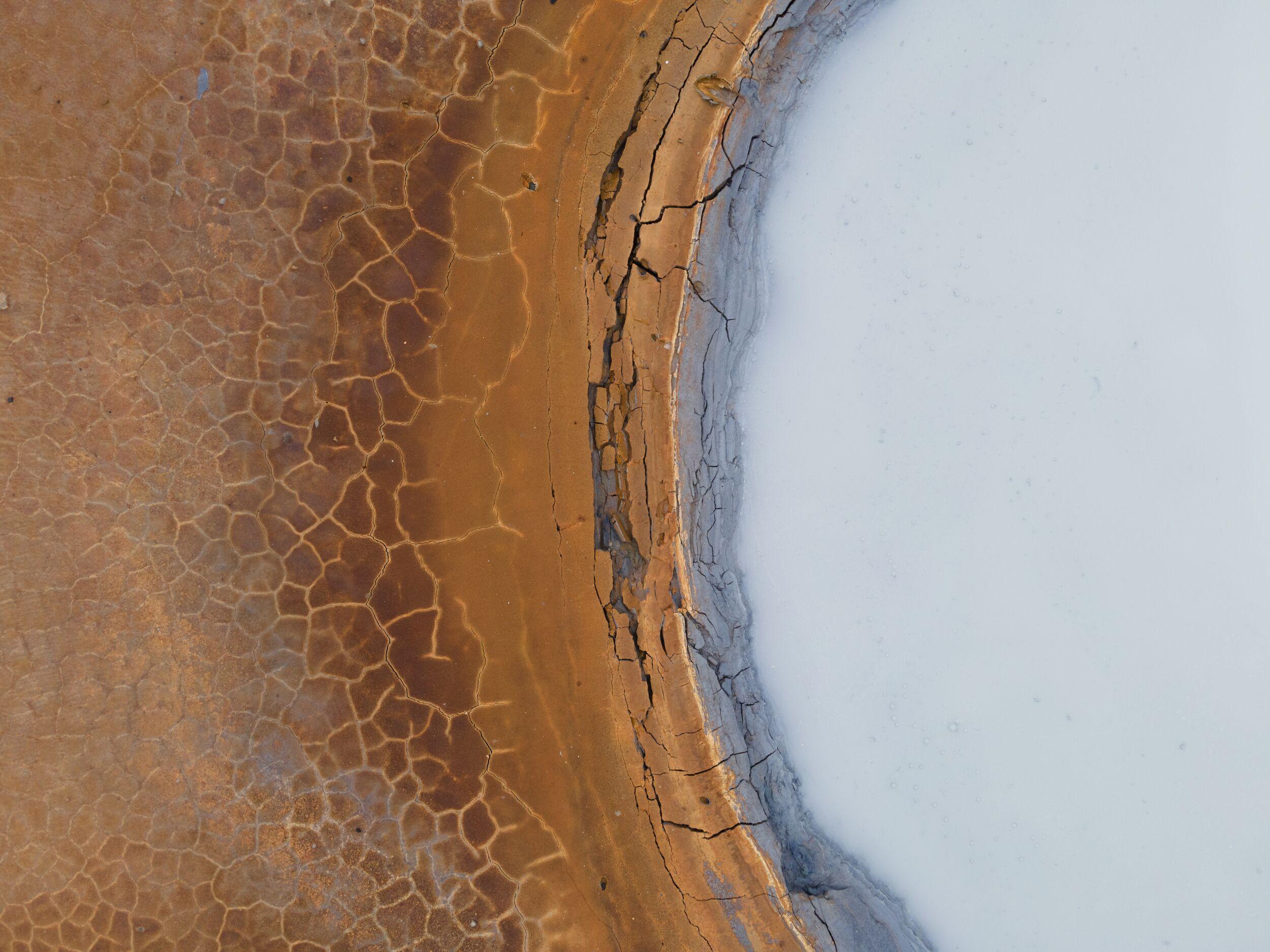 Close aerial view of cracked mineral crust and pale geothermal water at Gunnuhver.