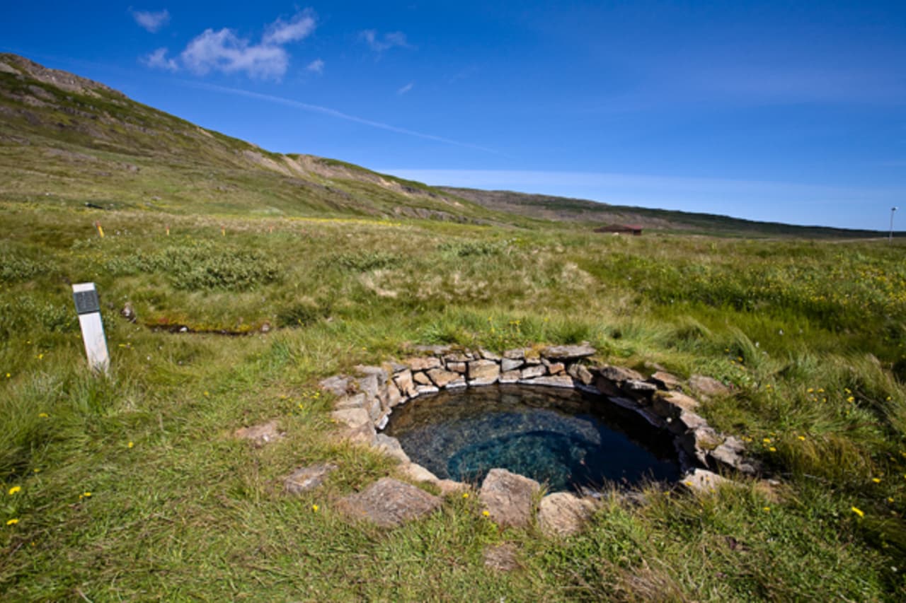 Stone-lined Gvendarlaug hot spring in the grassy Bjarnarfjörður valley.