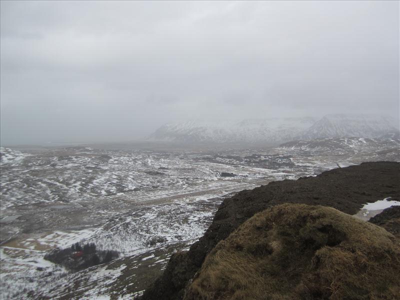 A dark Hafrafell edge overlooking snowy Mosfellsbær terrain and low cloud.