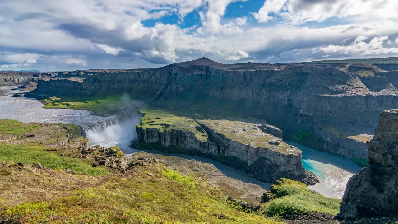 Hafragilsfoss and the Jökulsá á Fjöllum canyon with cliffs, river bends, and summer vegetation.