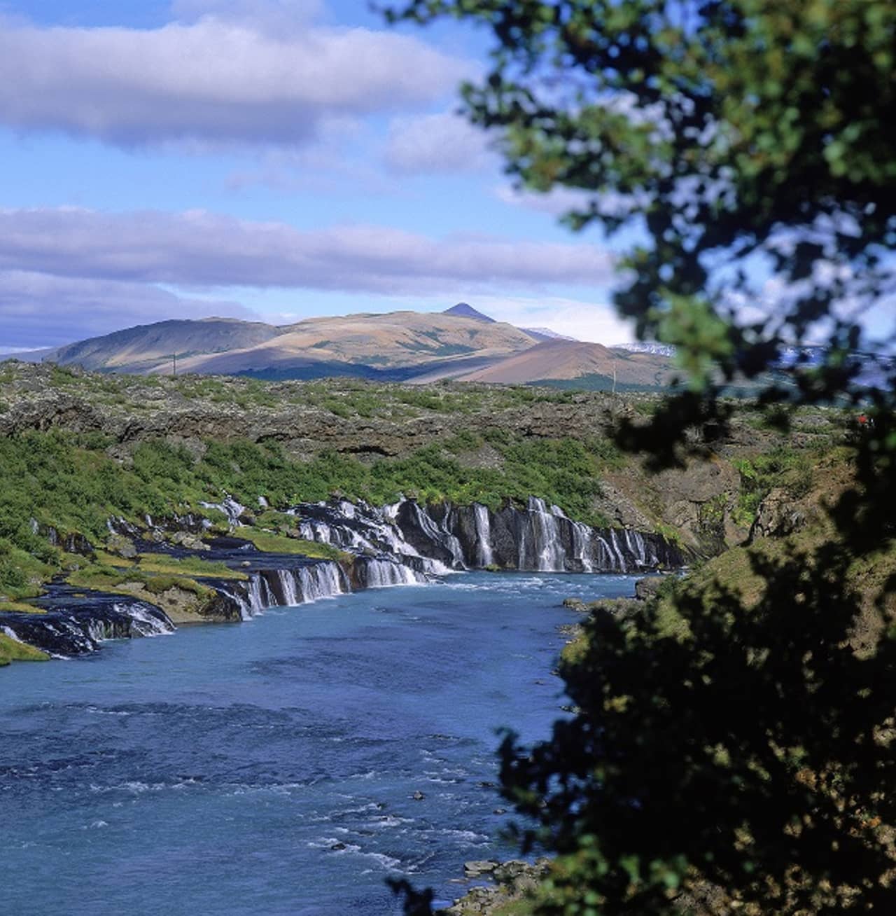 Hraunfossar waterfalls below the Hallmundarhraun lava field with mountains beyond in West Iceland.