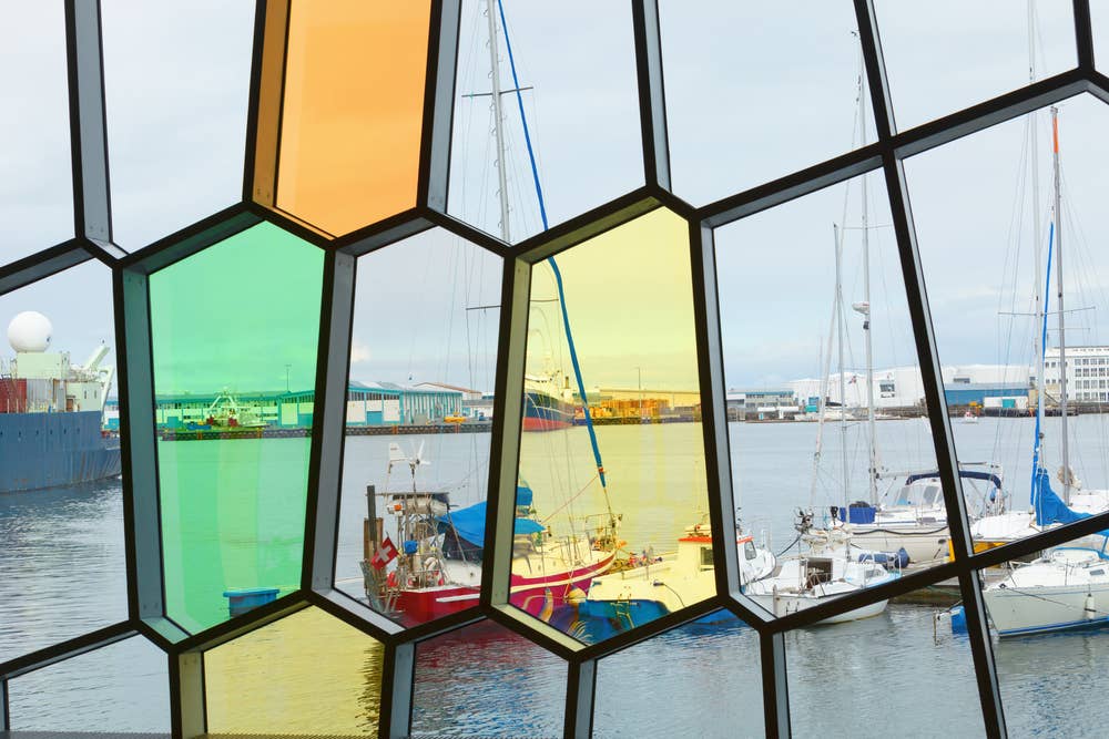 Colored glass panels inside Harpa framing boats in Reykjavík old harbor