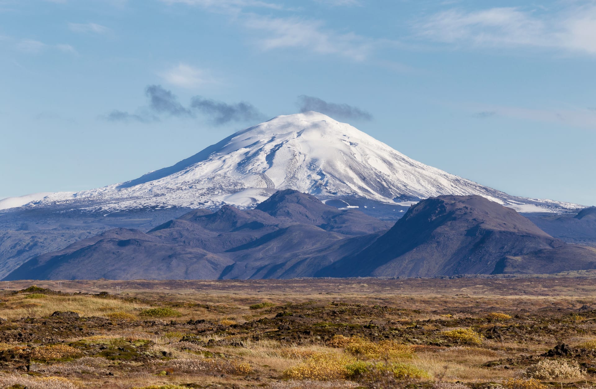 Snow-covered Hekla rising above dark lava fields and low volcanic hills in South Iceland.