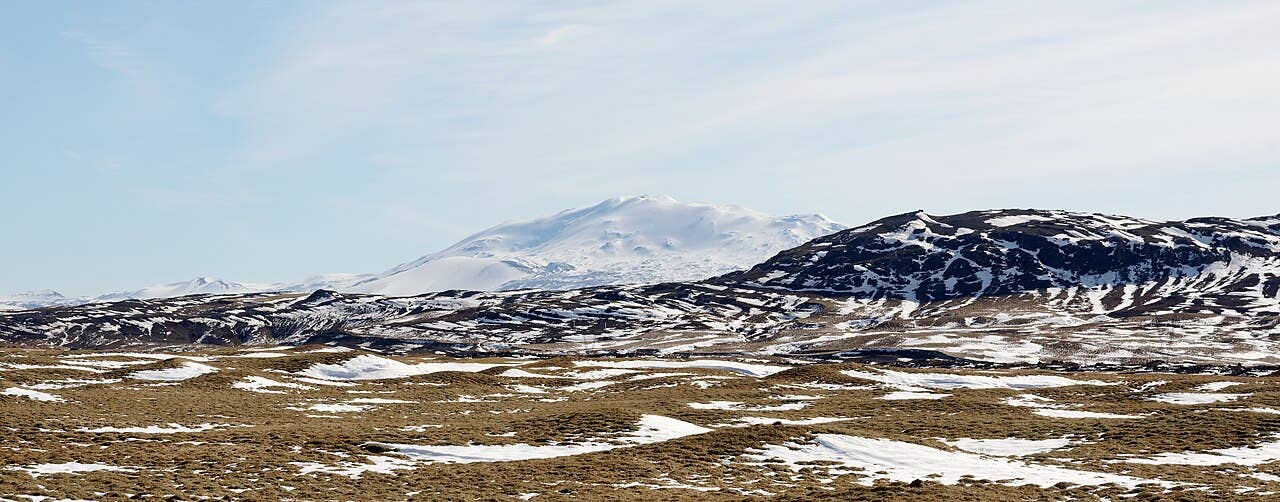 Hekla volcano seen across snowy lava fields and low hills from Road 32 in South Iceland.