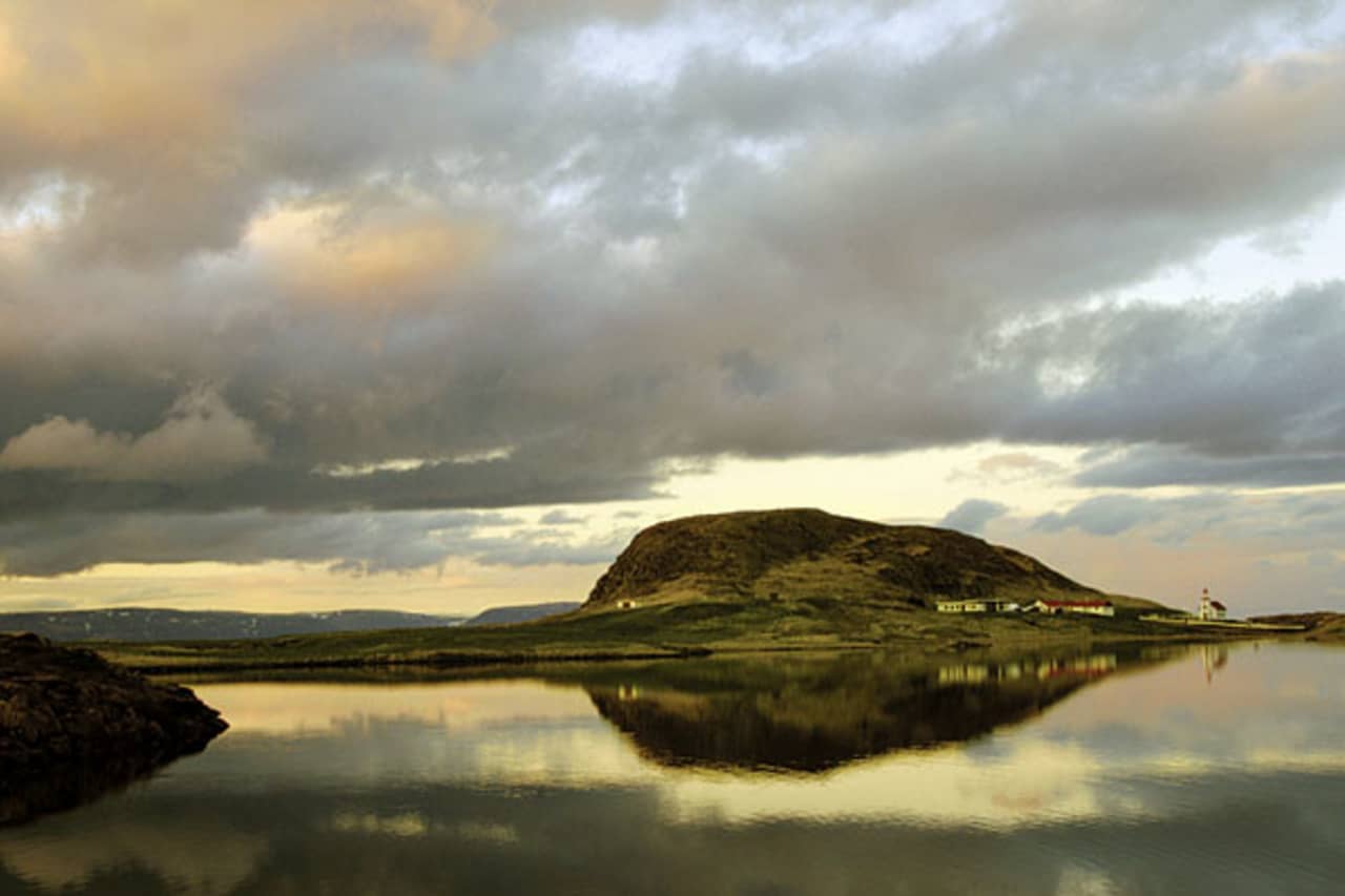 Helgafell reflected in still water with Helgafell church at the base of the mountain.