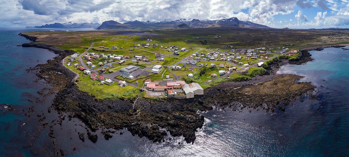 Aerial view of Hellissandur village between rocky shoreline and Snæfellsnes mountains.