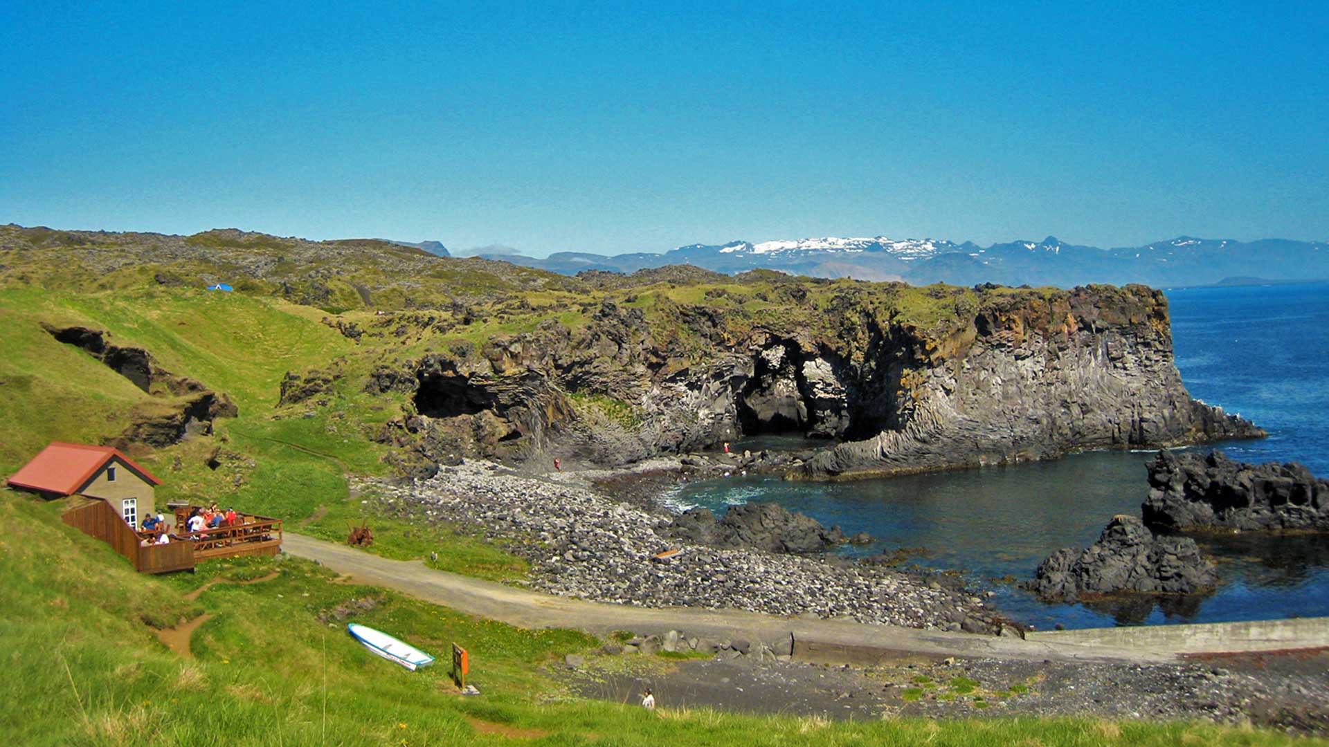 Hellnar shoreline with black lava cliffs, a small seafront building, and the Atlantic below Snæfellsnes.