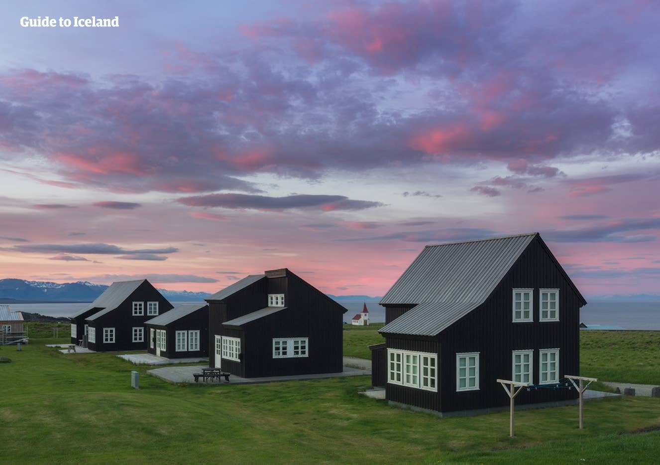 Historic Hellnar village buildings and grassy shore below Snæfellsnes mountain scenery.