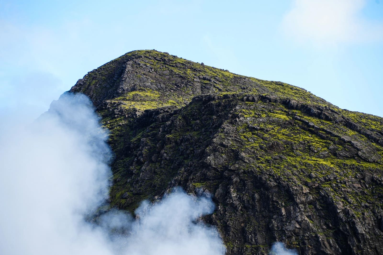 Steam drifting across a green and black Hengill mountain slope near the geothermal area.
