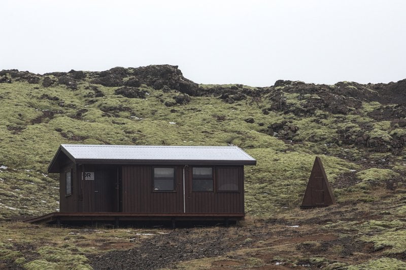 Múlasel hut in the Hengill area beside dark lava ground and mossy slopes.