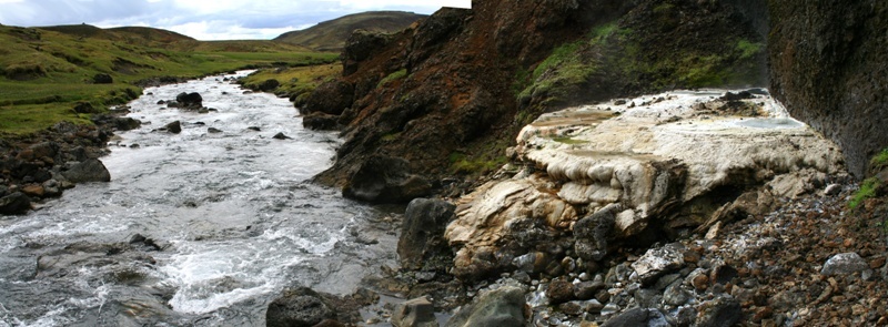 Hengladalir river water flowing beside pale geothermal deposits and green valley slopes.