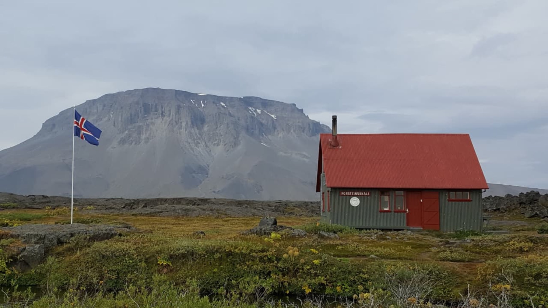 Þorsteinsskáli hut at Herðubreiðarlindir with Herðubreið rising behind it in cloudy weather.
