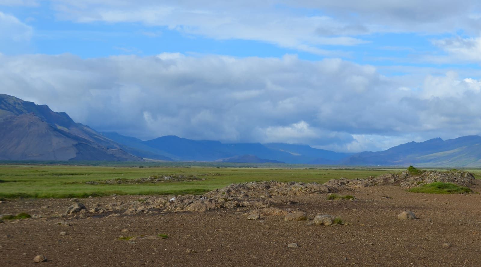 Wide view across Hítardalur valley with lava ground, green lowland, mountains, and clouds in West Iceland.