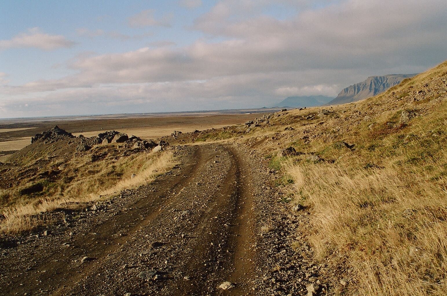 A narrow track crossing rough ground toward the open Hítardalur valley and distant cliffs.
