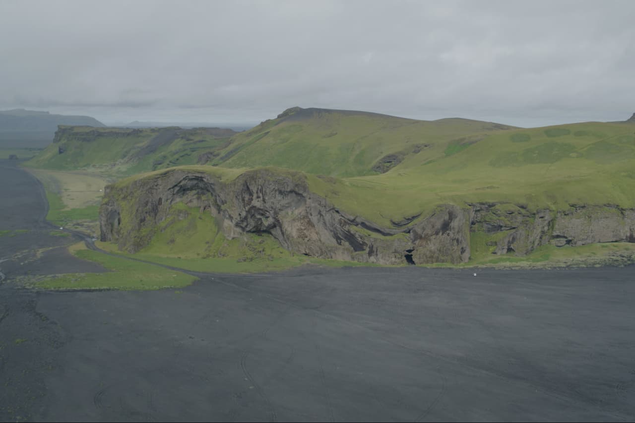 Steep green slopes and dark cliffs at Hjörleifshöfði above the South Coast sandplain