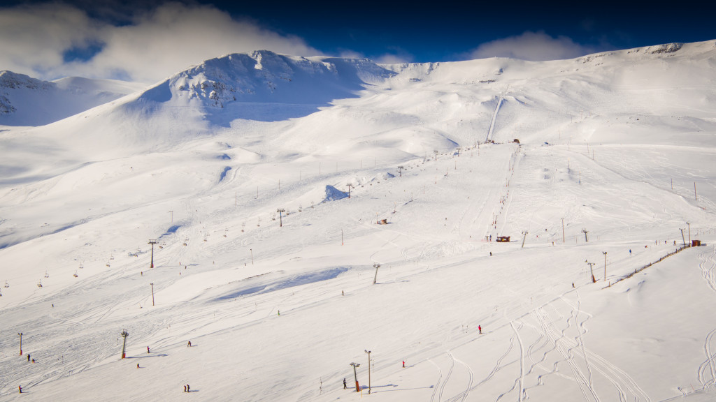 Snowy Hlíðarfjall ski slopes and mountain face above Akureyri under bright winter cloud.