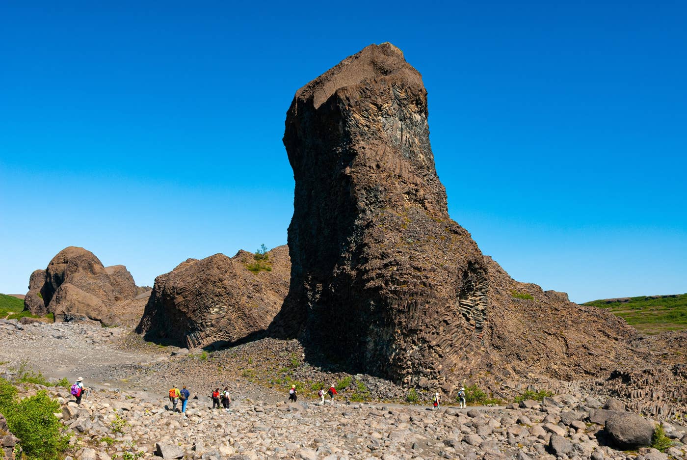 Tall basalt spire and visitors on a marked path at Hljóðaklettar.