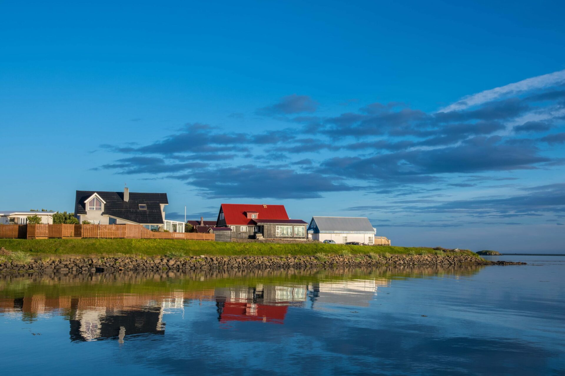 Colorful houses reflected in still water along the Höfn shoreline.