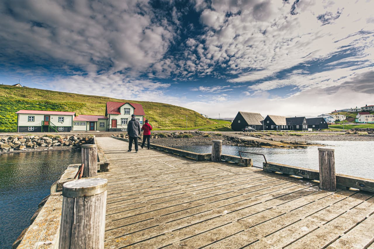 Wooden harbor pier in Hofsós with village buildings and Skagafjörður hills behind it.