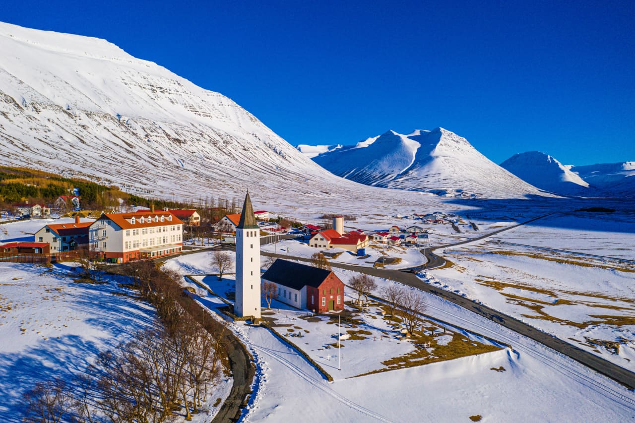 Hólar Cathedral and school buildings in Hjaltadalur surrounded by snow-covered mountains.
