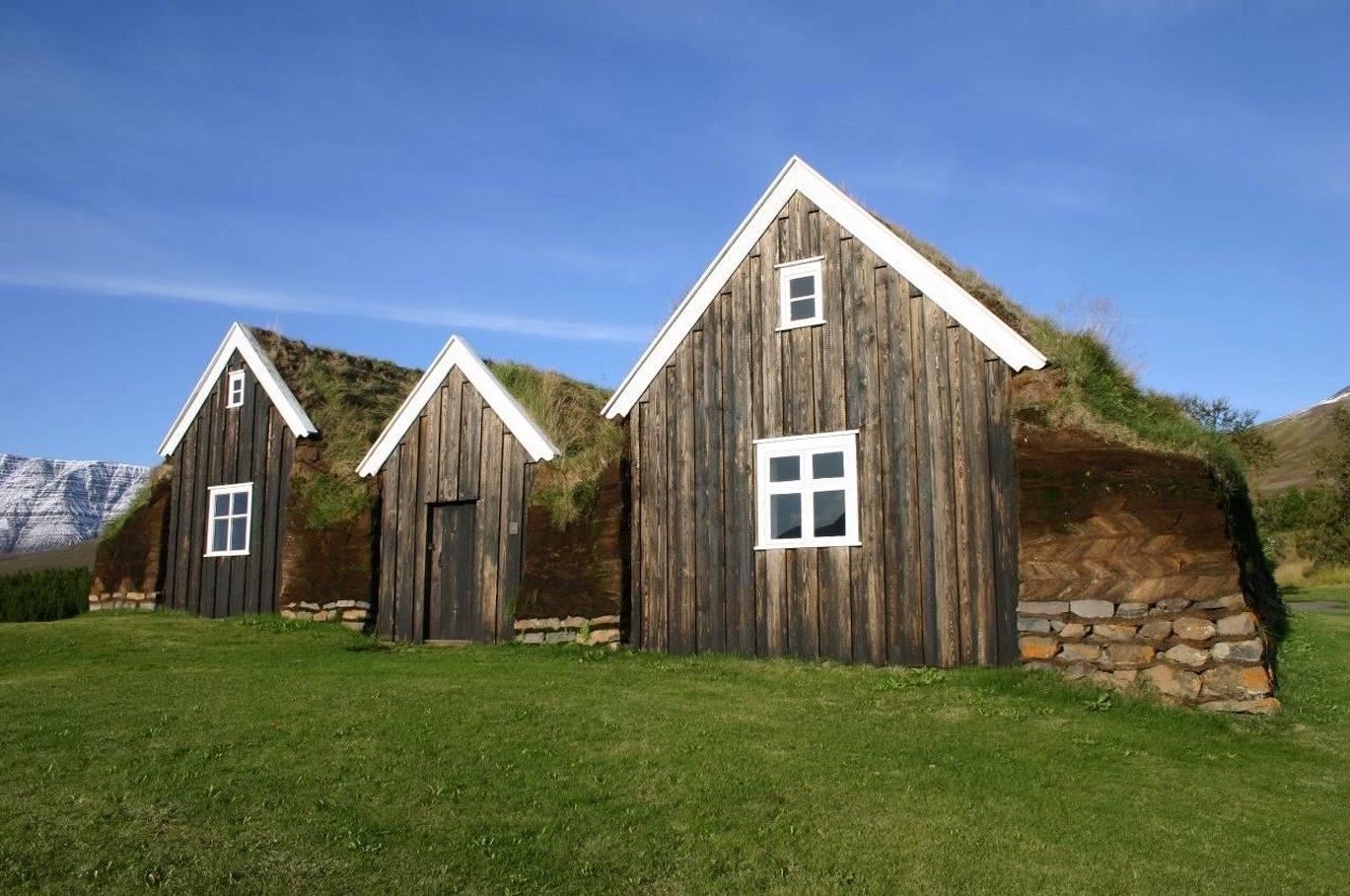 Nýibær turf house at Hólar in Hjaltadalur with timber gables, turf walls, and mountains behind it.