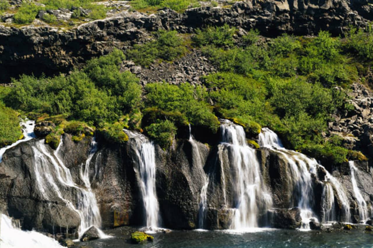 Detailed view of Hraunfossar streams falling from lava rock into blue-green water.