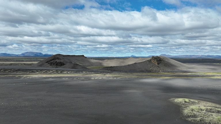 Hrossaborg crater rising from black sand plains under broken cloud.