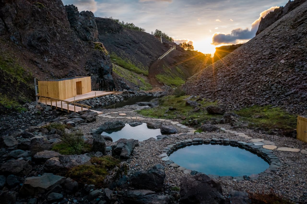 Stone hot pools and wooden changing structures in a narrow rocky canyon at Húsafell Canyon Baths.