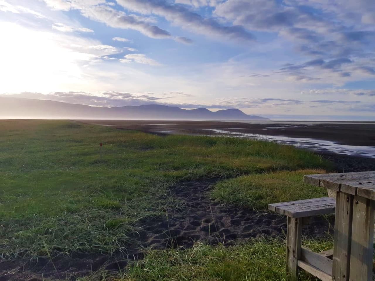 Black sand, grass, and broad coastal flats at Húsey with East Iceland mountains across the water.