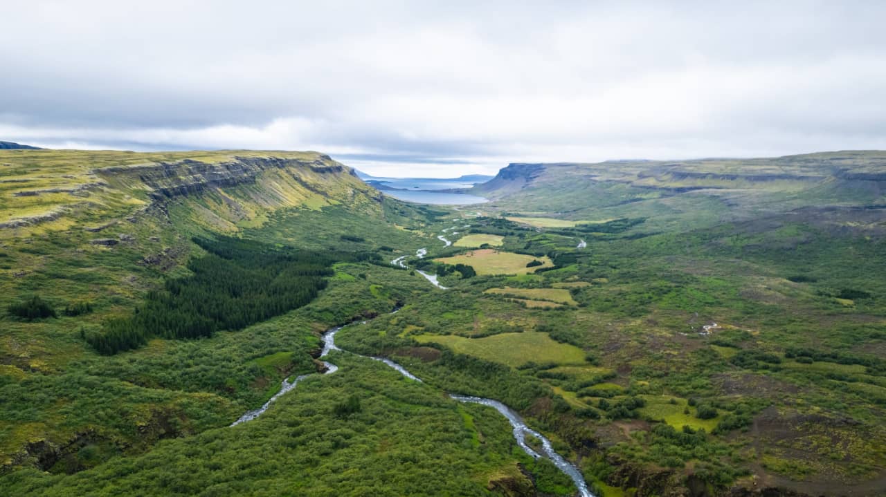 Botnsdalur valley opening toward Hvalfjörður with streams, green slopes, and fjord water in the distance.