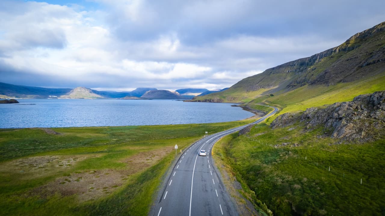 Road 47 curving along Hvalfjörður below green hills and wide fjord water.