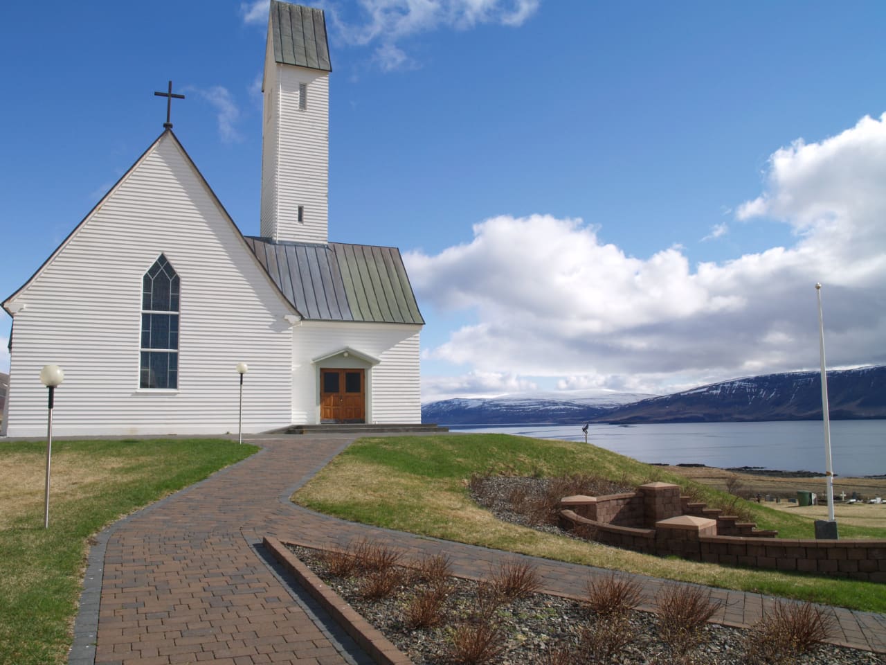 A white church beside Hvalfjörður with the fjord and snow-streaked mountains behind it.