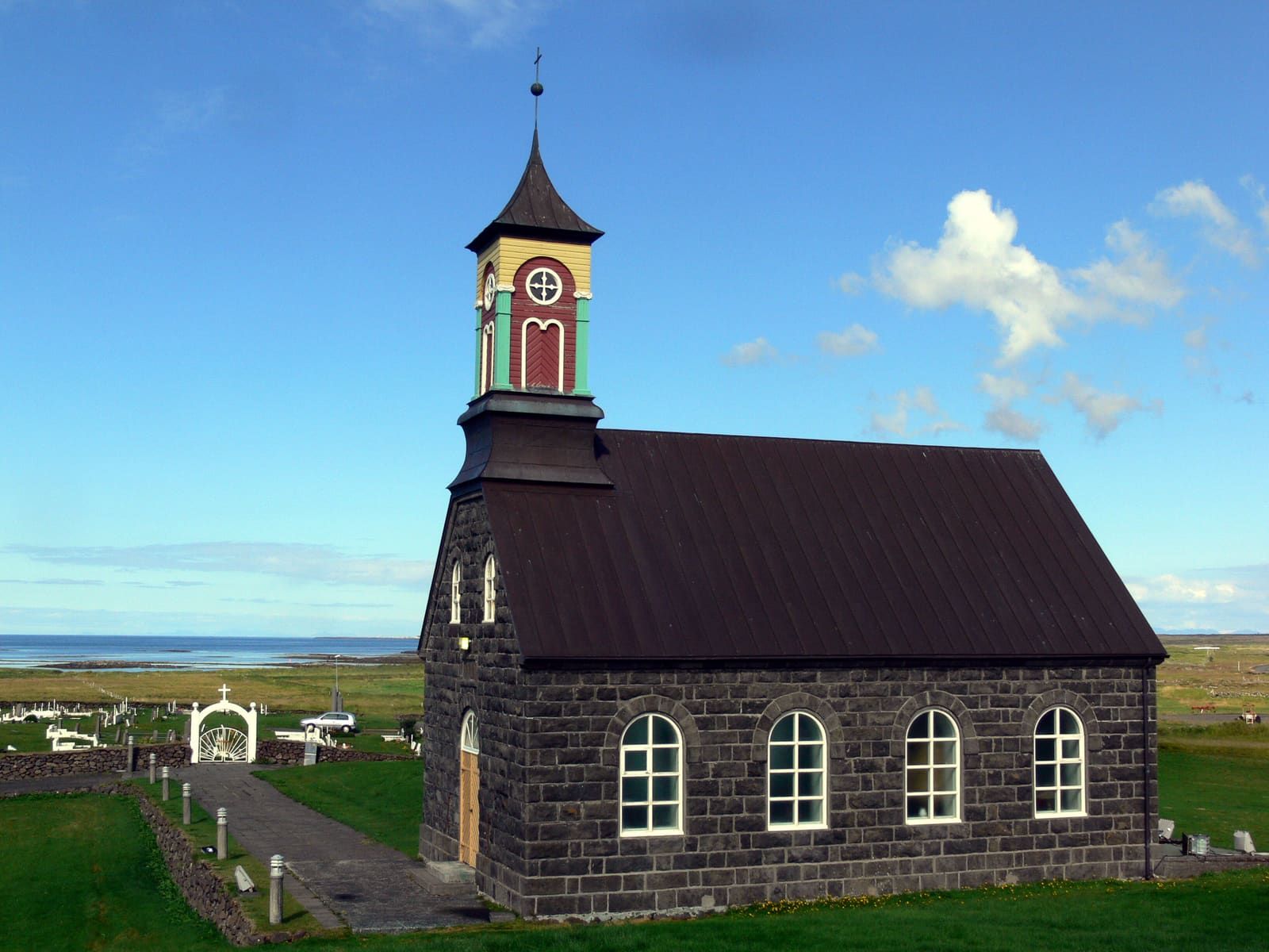 Stone walls and tower detail on Hvalsneskirkja with the Reykjanes coast visible beyond the churchyard.