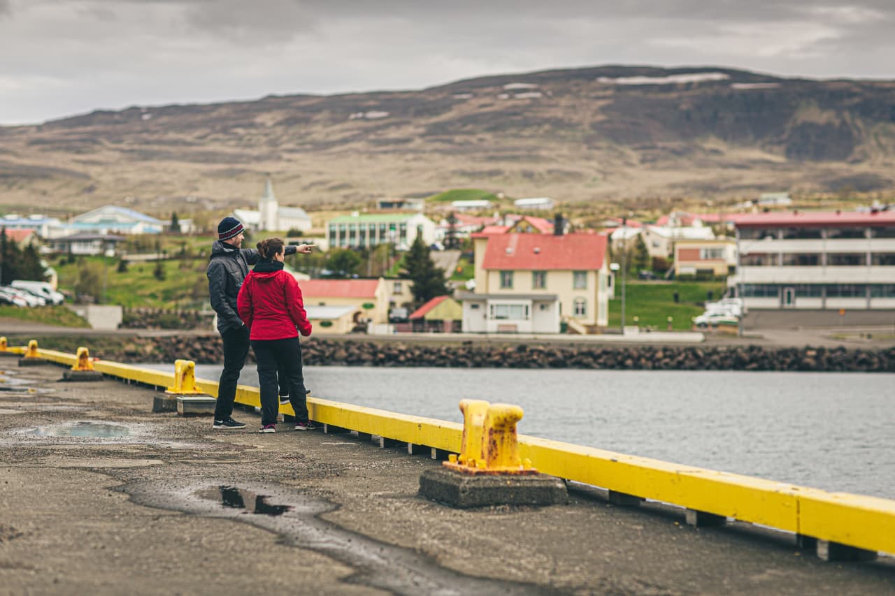Visitors standing on the Hvammstangi harbor quay with the town behind them