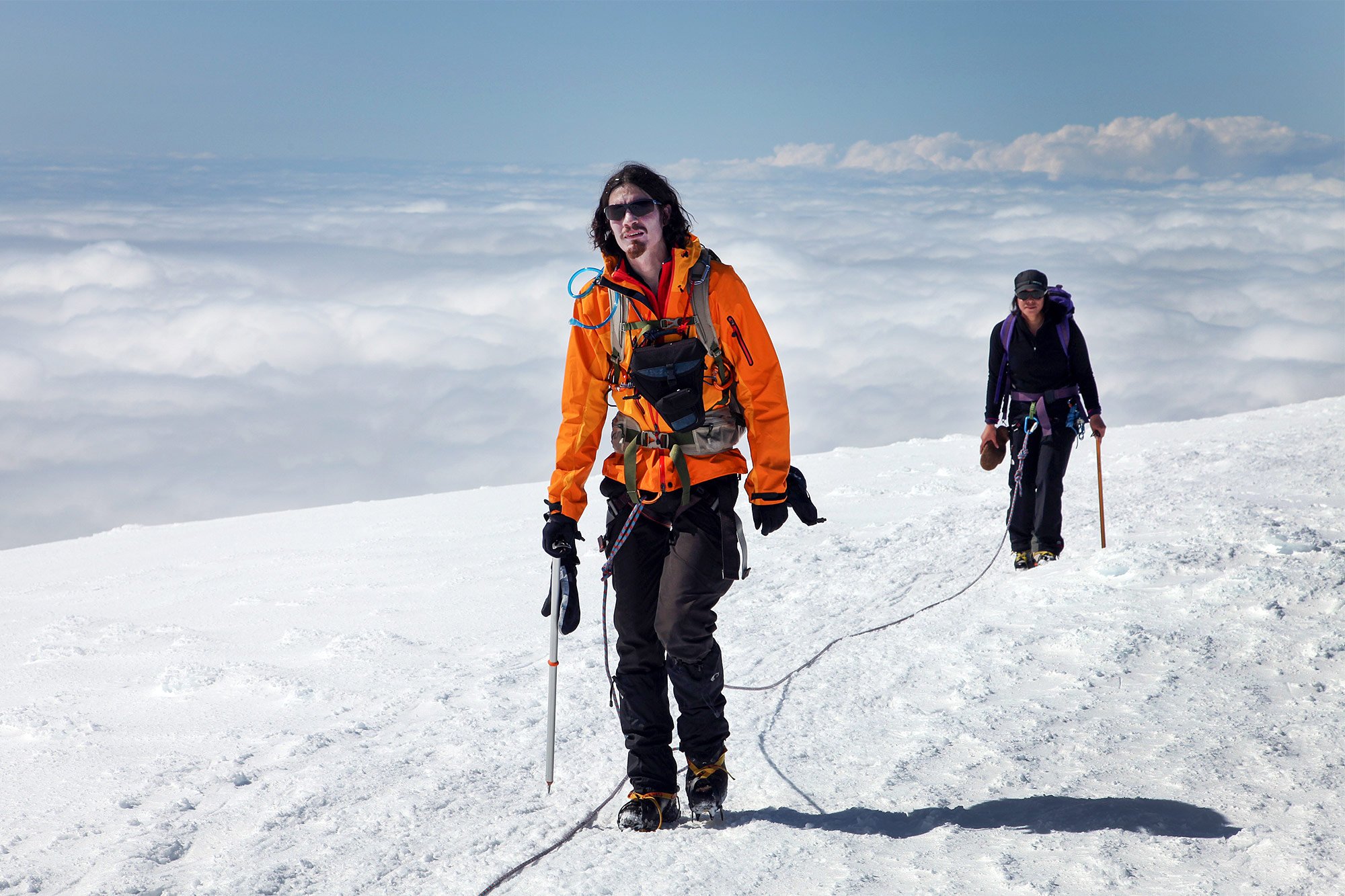 Two roped climbers crossing a bright snow slope high on Hvannadalshnúkur.
