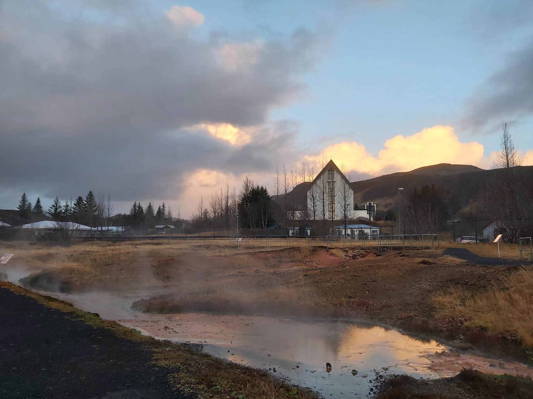 Steam rising near buildings and hills in Hveragerði during soft evening light.