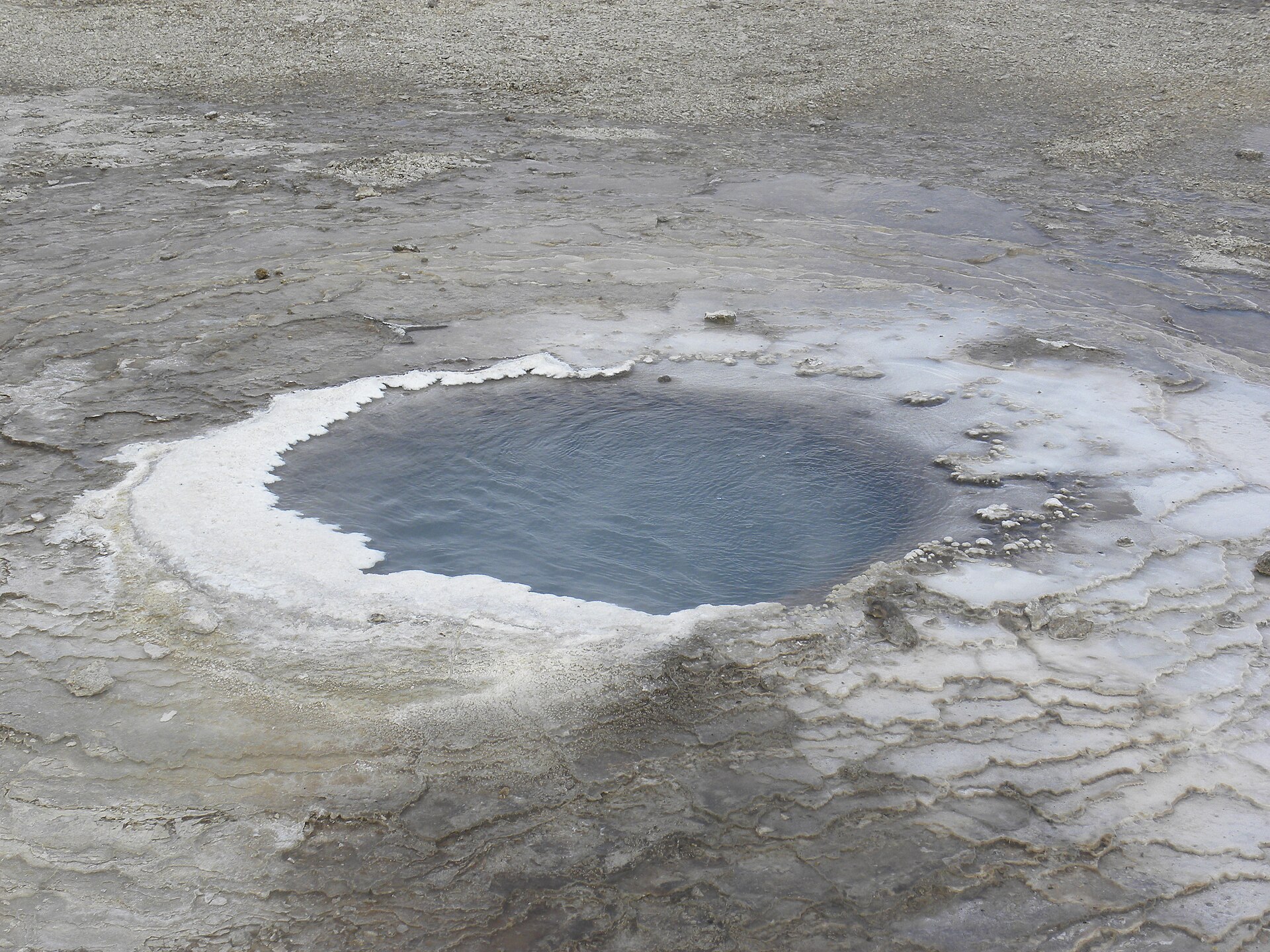 A close mineral-edged hot spring pool at Hveravellir with pale geothermal crust around dark water.