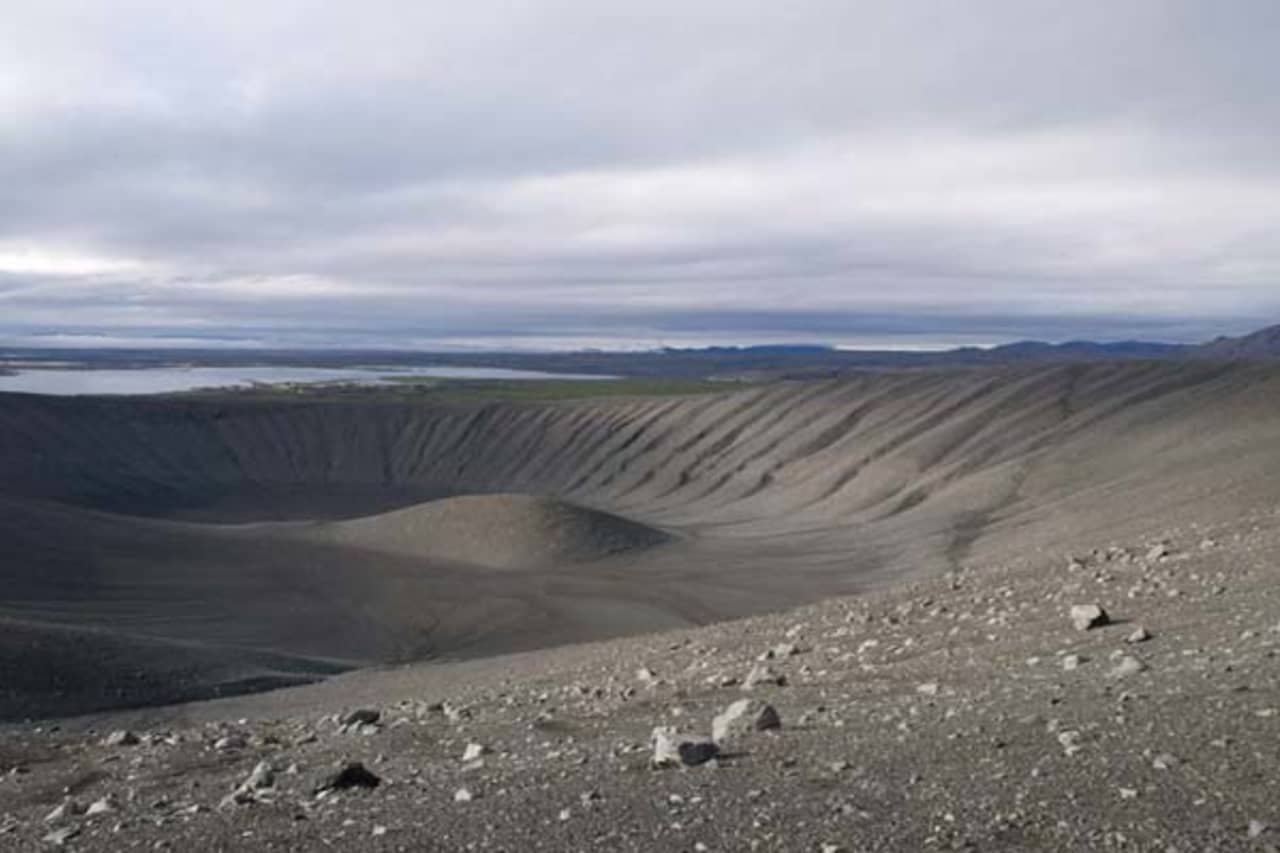 Visitors walking on the rim of Hverfjall crater with dark volcanic slopes around the trail.
