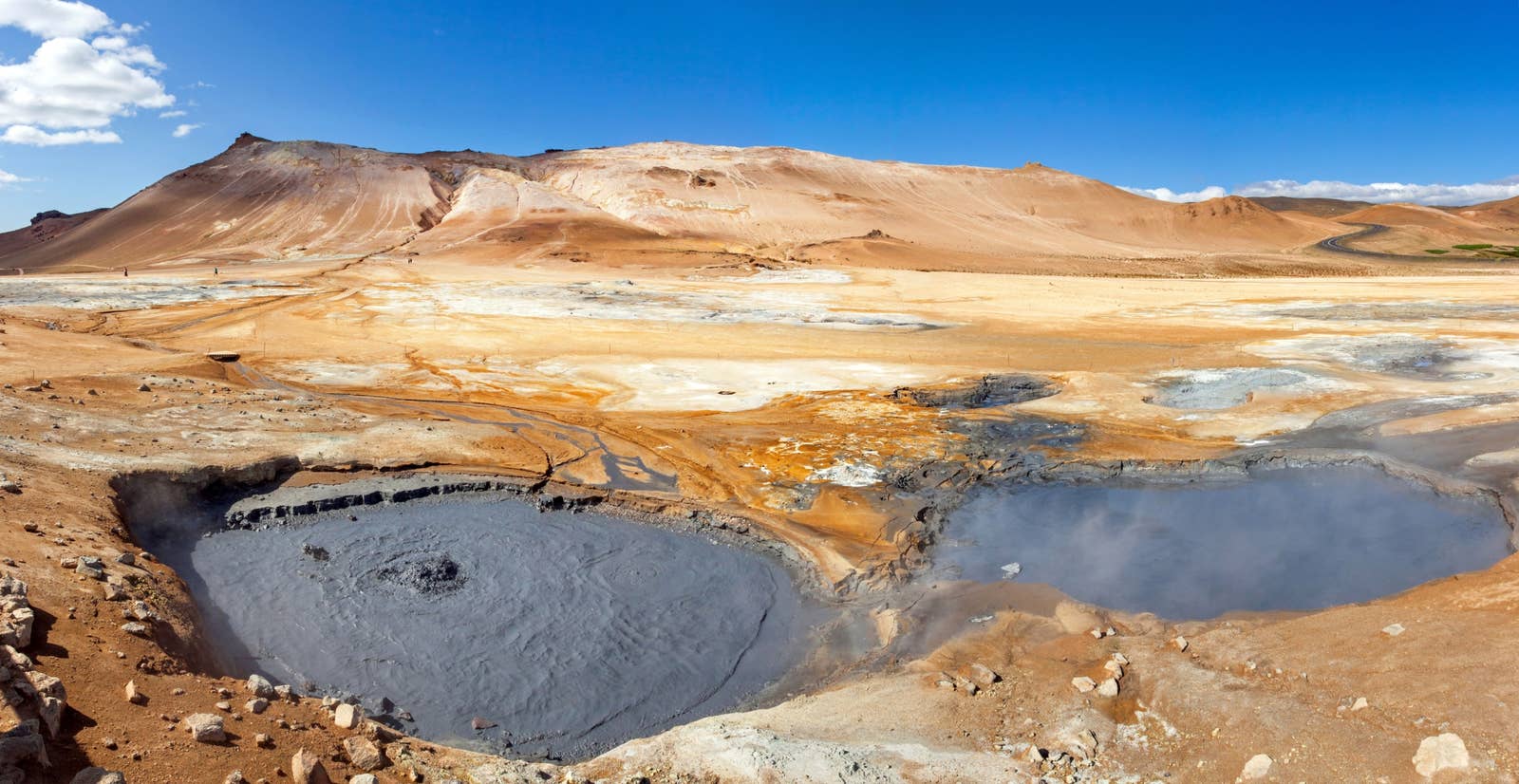 Wide mud pools and pale mineral ground at Hverir with the Námafjall ridge behind them.