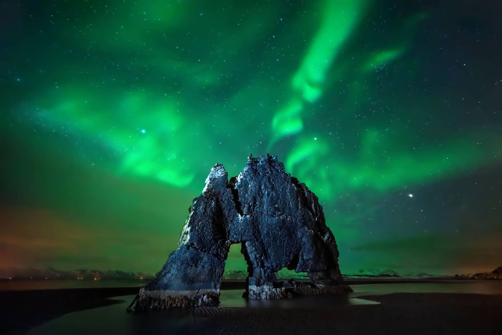 Northern lights glowing above Hvítserkur on a dark winter coast.