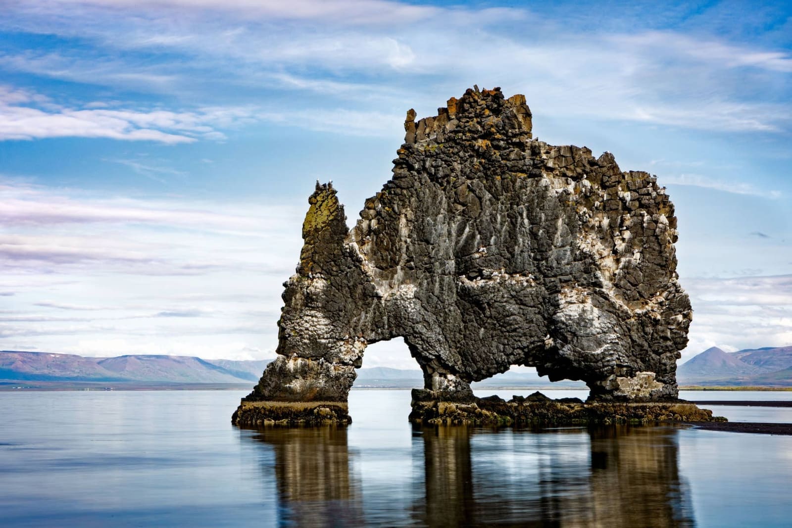 Hvítserkur reflected in calm water below a pale sky.