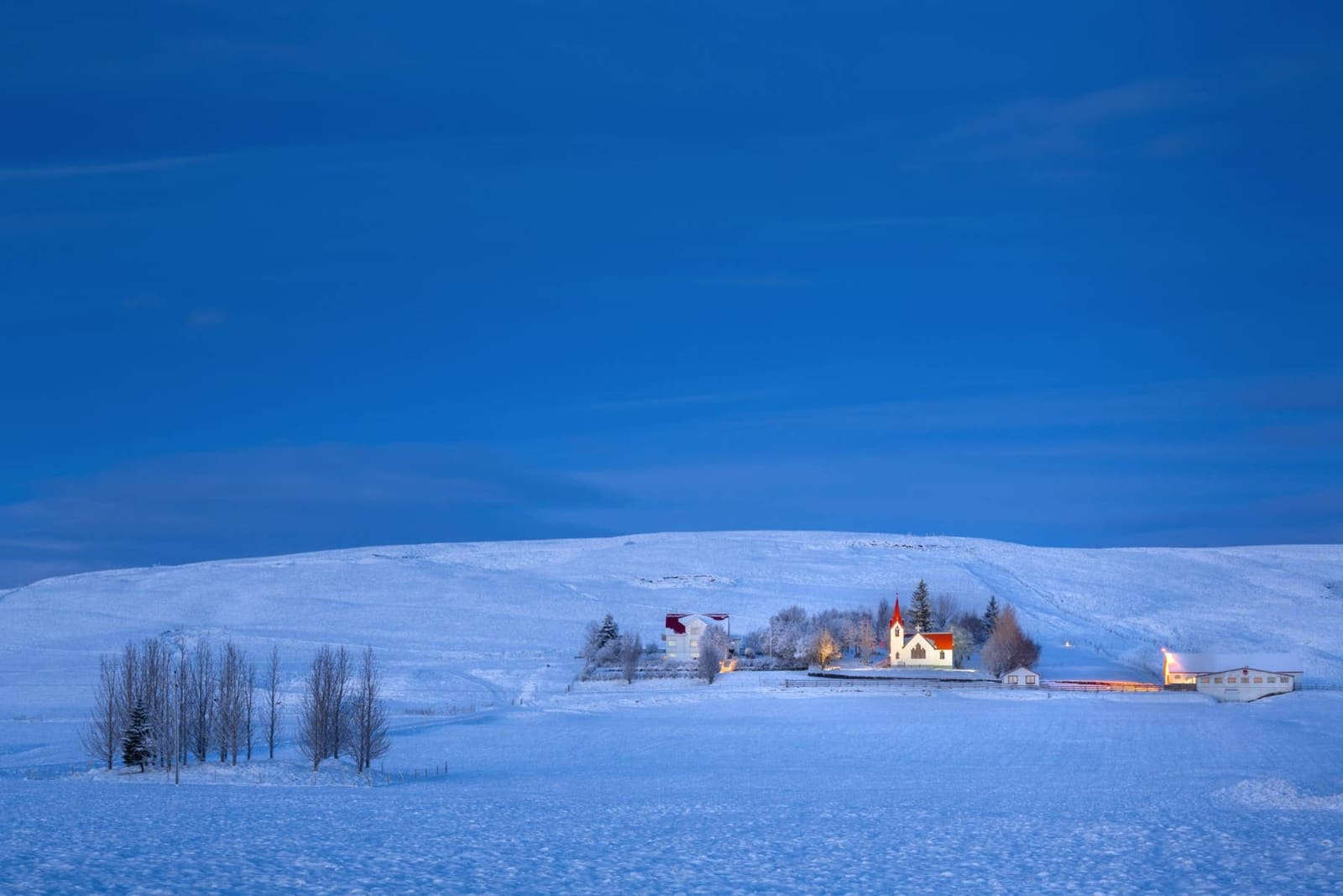Snowy view of Hvolsvollur with houses, church, and open South Iceland fields at dusk.