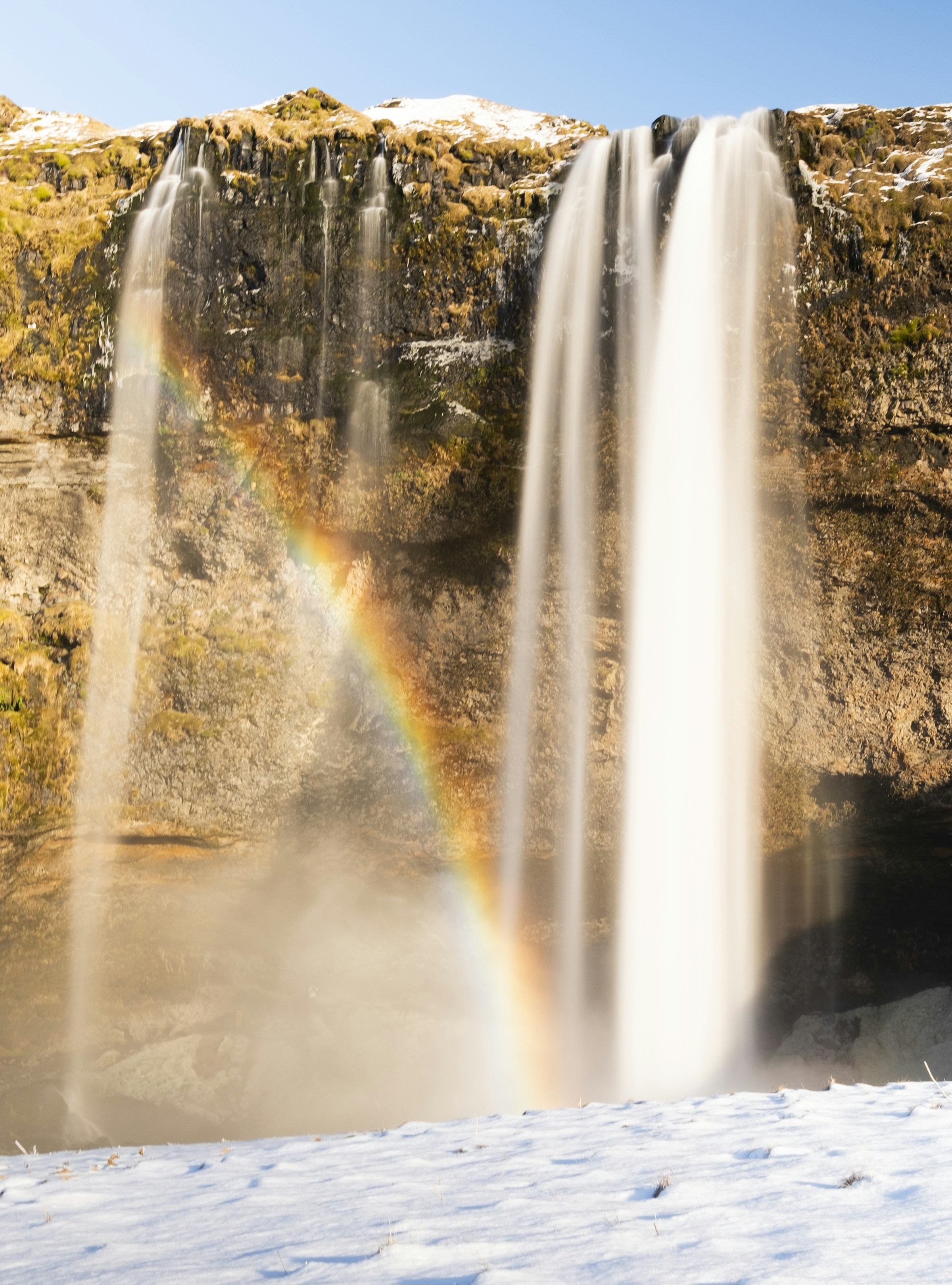 Rainbow and snow around Írárfoss waterfall in a narrow South Iceland gorge.